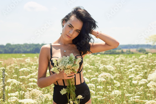 Young brunette girl among the flower field holding a bouquet, enjoying life. Beauty of nature. Freedom concept. Rural landscapes in bright sunlight. Wheat field ears background.
