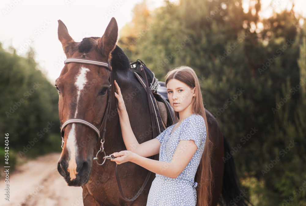 Obraz premium A beautiful young girl with long hair stands next to a horse in nature in the summer