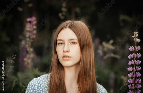 A young beautiful girl with long red hair in a clearing among the flowers. Lupines