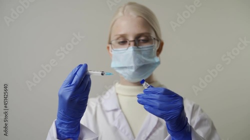 A young woman doctor in glasses and a medical mask draws saline from a glass ampoule into a syringe. Vaccination and Medicine. Health and treatment. Close-up, slow motion, HD. photo