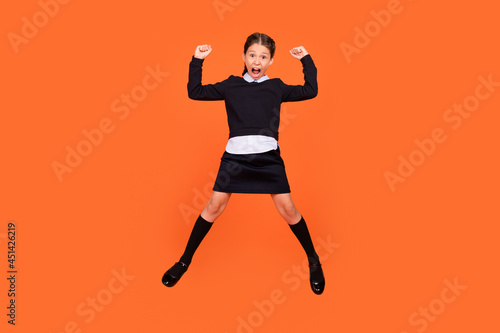 Full length photo of young girl happy positive smile celebrate victory success fists hands jump isolated over orange color background