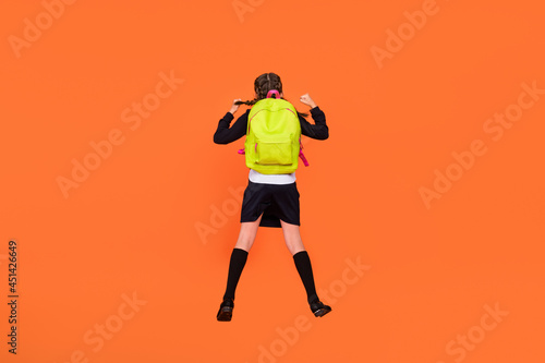 Back rear spine view photo of small girl jump up wear backpack winner victory isolated on orange color background © deagreez