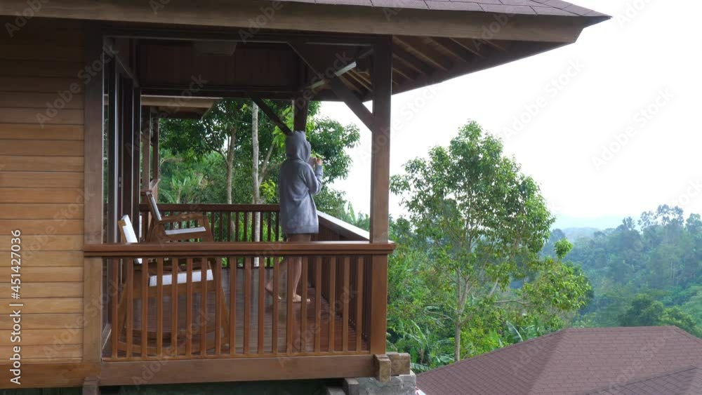 Person standing on a balcony looking at the garden holding cup of tea. Morning nature concept