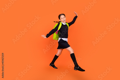 Full length body size view of nice pretty funky cheerful schoolgirl jumping walking isolated over bright orange color background © deagreez