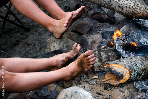 Children warm their dirty feet after swimming on campfire at campsite. Barefoot children s legs warming themselves by the fire.