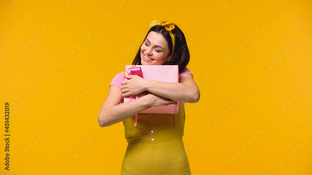 Happy woman hugging present isolated on yellow. Happy woman hugging present isolated on yellow.