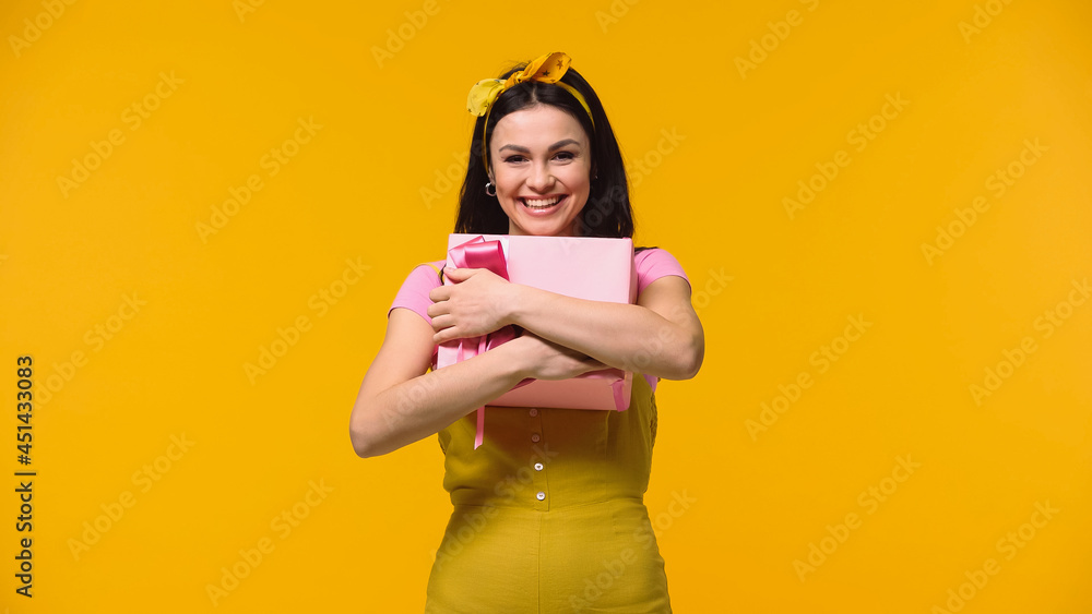 Woman smiling at camera while hugging gift box isolated on yellow. Woman smiling at camera while hugging gift box isolated on yellow.