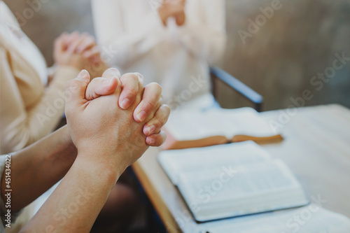 Close up of a Christian man and woman hands praying with friends over wooden table, Christian group study bible and pray together, Spirituality background with copy space
