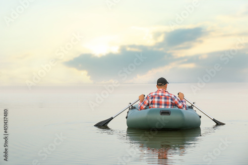Man rowing inflatable rubber fishing boat on river, back view. Space for text