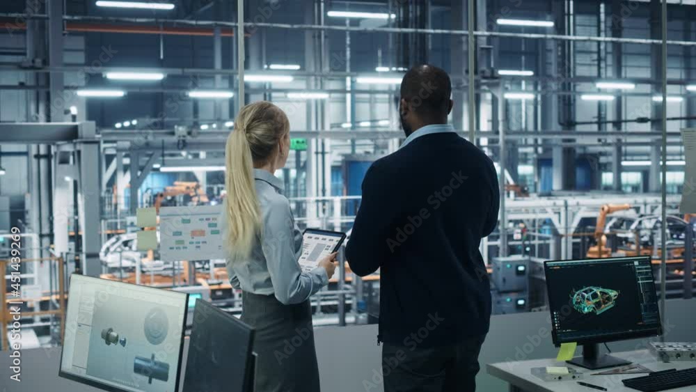 Car Factory Office: Female Engineer Talks with Male Scientist, Use Tablet Computer to Design Production Conveyor for Advanced Power Engines. Automated Robot Arm Assembly Line Manufacturing Vehicles Car Factory Office: Female Engineer Talks with Male Scientist, Use Tablet Computer to Design Production Conveyor for Advanced Power Engines. Automated Robot Arm Assembly Line Manufacturing Vehicles