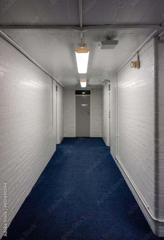Basement corridor with white tiled walls and blue carpet.