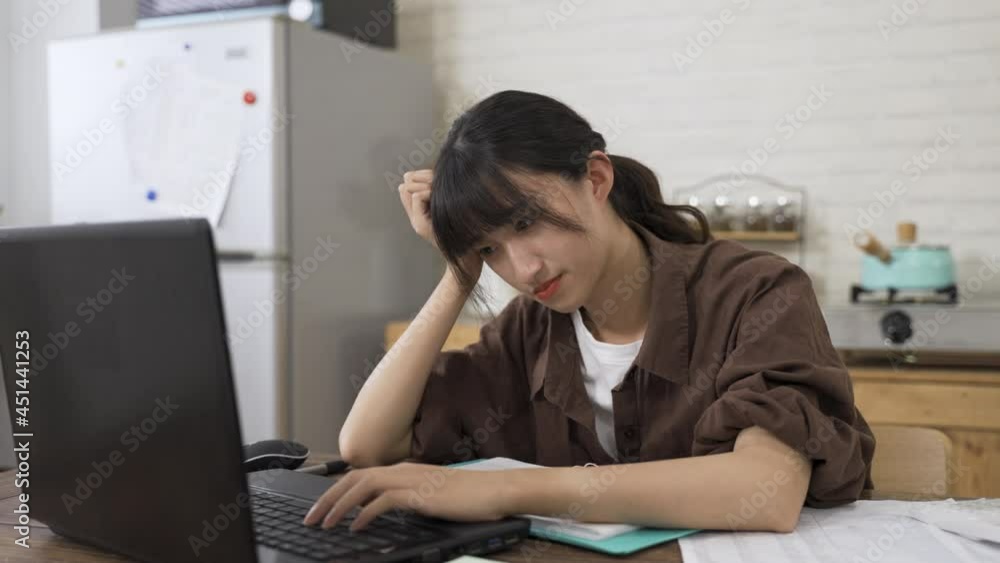 japanese female freelance worker propping head is having trouble thinking of good ideas while working from home on the computer in the dining room at daytime. japanese female freelance worker propping head is having trouble thinking of good ideas while working from home on the computer in the dining room at daytime.