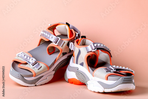 Women's, fashionable, sports sandals with orange accents on a pink background. New youth shoes for girls. Front view.