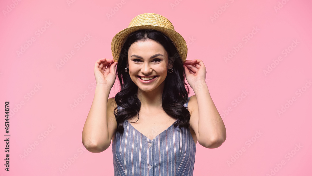 Pretty woman smiling at camera while holding sun hat isolated on pink. Pretty woman smiling at camera while holding sun hat isolated on pink.