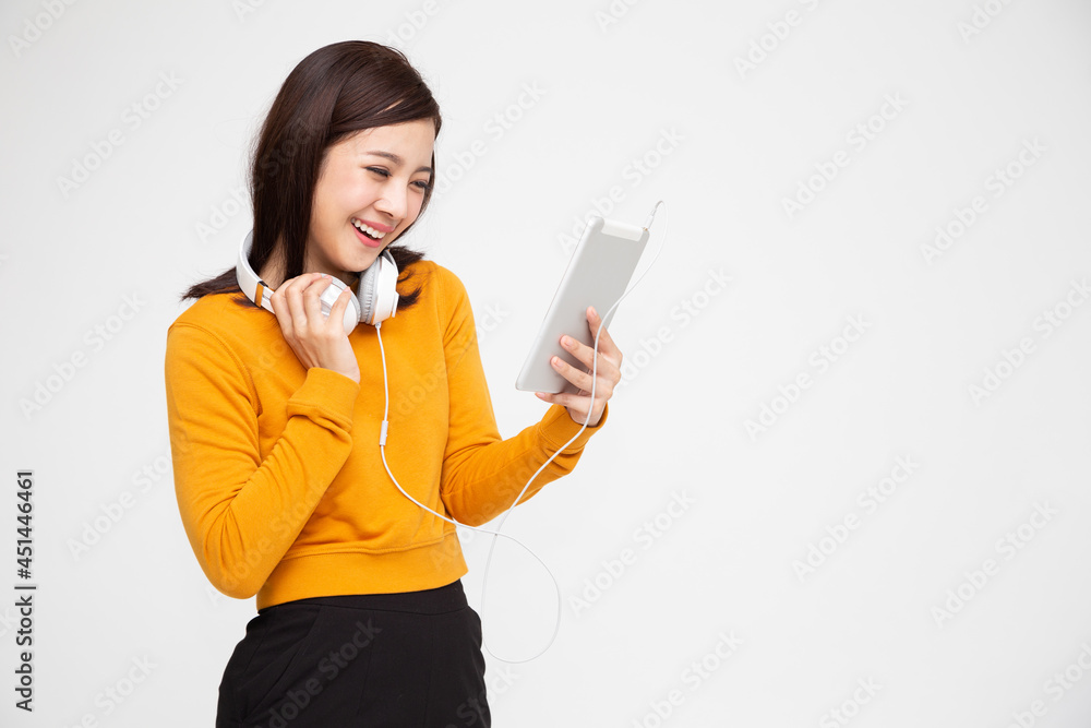 Happy Asian female with headphones smiling and browsing social media on tablet while looking at screen isolated on white background Happy Asian female with headphones smiling and browsing social media on tablet while looking at screen isolated on white background
