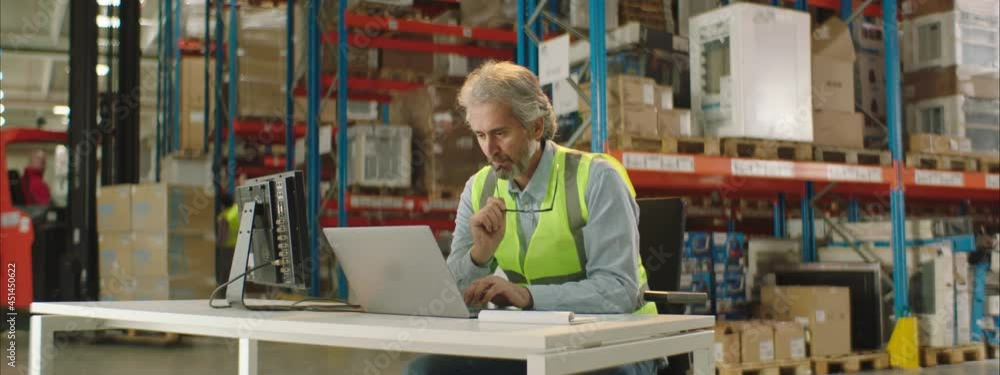 Warehouse worker or manager working on his laptop computer while sitting at a desk. Warehouse worker or manager working on his laptop computer while sitting at a desk.