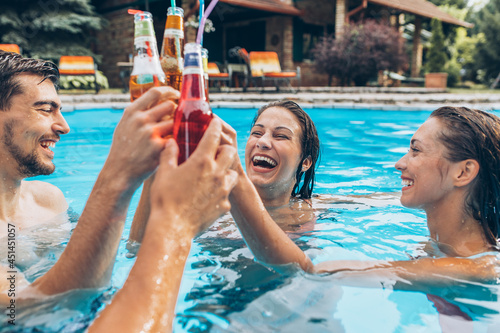 Group of young people refreshing in a swimming pool and toasting together with a cold drink.	