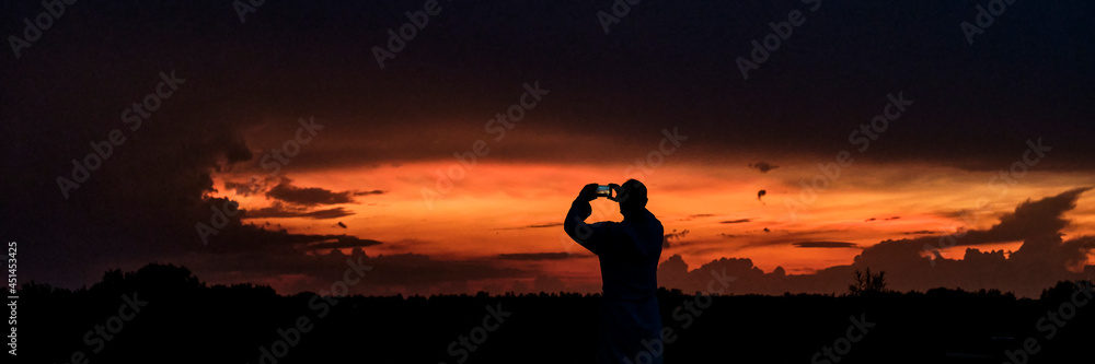 Silhouette of man taking pictures on mobile phone beautiful dramatic sunset.