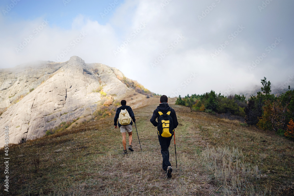 Two man friends with backpack hiking together in autumn nature. Male backpacker relax and enjoy walking on mountain trail. Healthy outdoor lifestyle holiday vacation concept.
