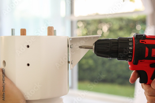 man assembling white table furniture at home using cordless screwdriver