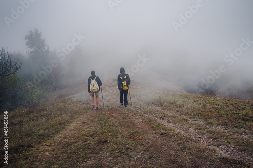 Two man friends with backpack hiking together in autumn fog nature. Male backpacker relax and enjoy walking on mountain trail. Healthy outdoor lifestyle holiday vacation concept.