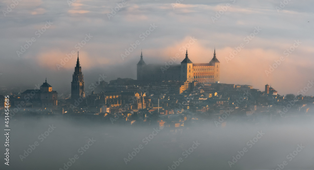 Aerial view of the old European city with the ancient castle Alcazar of Toledo and cathedral tower in the mist in colorful sunrise, Toledo, Spain