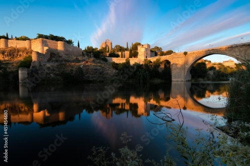 Panoramic view of the Tajo river, San Juan de los Reyes church and San Martin bridge of the old European city in a colorful sunset, Toledo, Spain.