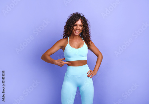 snapshot of happy cheerful expressive and satisfied black african american woman. woman dressed in trendy tracksuit. the woman points to her abdominal muscles