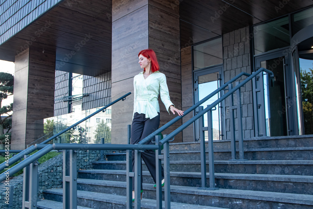 beautiful business girl with red hair walks through the city streets

