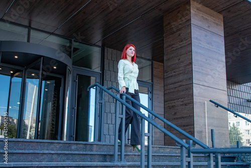 beautiful business girl with red hair walks through the city streets 