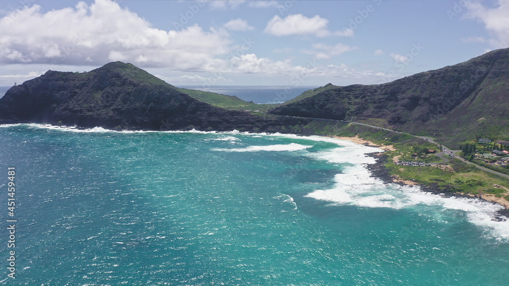 Flying over Makapuu Beach Park. Giant waves foaming and splashing in the ocean. The turquoise color of the Pacific Ocean water on tropical island. Magnificent mountains of Hawaiian island of Oahu.