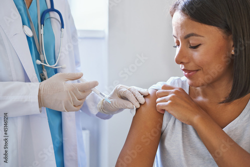 Young afro american woman receiving injection of coronavirus vaccine during appointment in clinic, doctor in uniform with syringe vaccinating female patient in hospital. Immunisation and vaccination