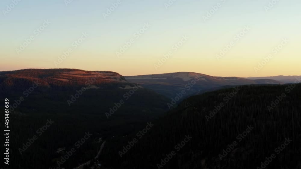Left tracking landscape aerial shot of a canyon in the Uinta Wasatch Cache National Forest in Utah with a highway below surrounded by pine trees and rocky mountains during a vivid summer sunset. Left tracking landscape aerial shot of a canyon in the Uinta Wasatch Cache National Forest in Utah with a highway below surrounded by pine trees and rocky mountains during a vivid summer sunset.