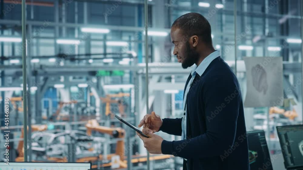 Car Factory Office: Portrait of Successful Black Male Chief Engineer Using Tablet Computer in Automated Robot Arm Assembly Line Manufacturing High-Tech Electric Vehicles. Elevating Tracking Shot Car Factory Office: Portrait of Successful Black Male Chief Engineer Using Tablet Computer in Automated Robot Arm Assembly Line Manufacturing High-Tech Electric Vehicles. Elevating Tracking Shot