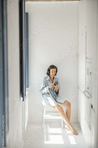 Young woman enjoys music in headphones while sitting alone in a bright room at home. Self-isolation and loneliness concept