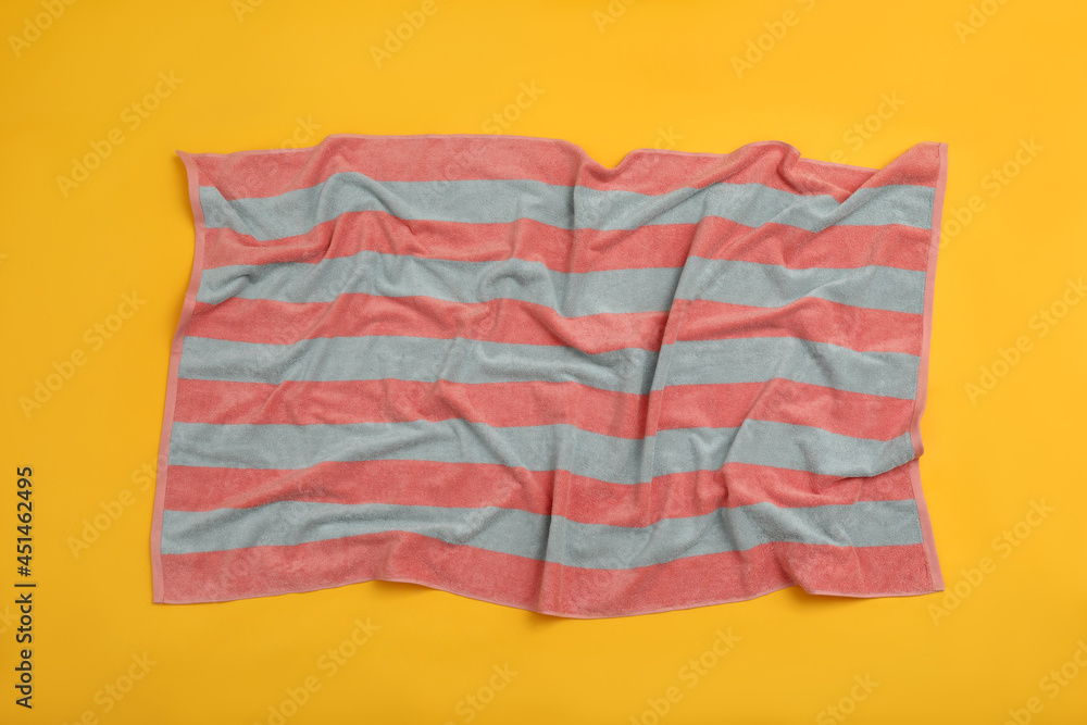 Crumpled striped beach towel on yellow background, top view