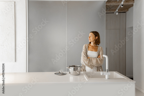 Portrait of a young woman standing in the modern white kitchen interior. Home comfort, lifestyle at home, modern and stylish interior