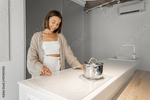 Young stylish woman cooking on induction hob at modern kitchen. Concept of smart technologies of kitchen appliances photo
