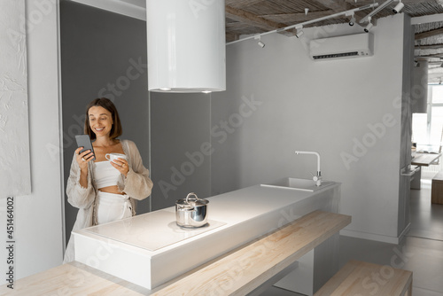 Woman with coffee cup and cell phone at modern kitchen interior in the morning