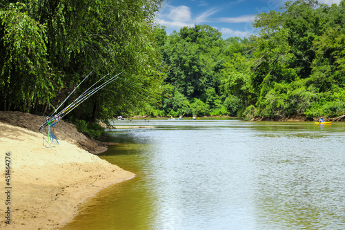 a gorgeous shot of the silky brown waters of the Chattahoochee river surrounded by green trees with blue sky and clouds with fishing poles on the banks at McIntosh Reserve Park in Whitesburg Georgia photo