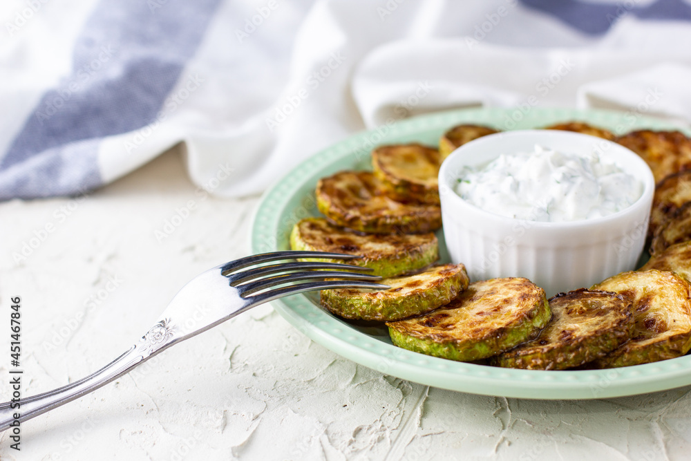 Fried slices of zucchini with sour cream sauce on plate. Fried courgettes with herb for dinner on white background Fried slices of zucchini with sour cream sauce on plate. Fried courgettes with herb for dinner on white background