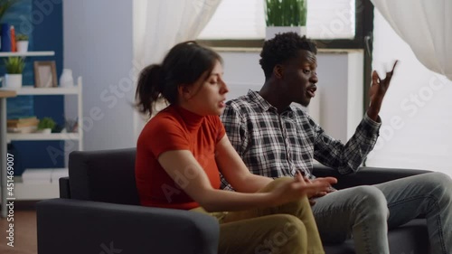 Angry interracial couple fighting on living room sofa. Married mixed race partners having argument about relationship problems and lifestyle. Irritated multi ethnic lovers yelling photo