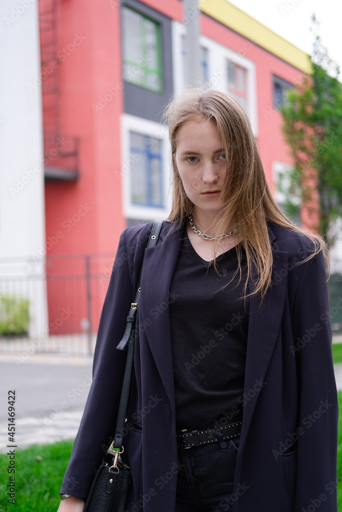 Fototapeta premium portrait of confident attractive brunette woman in black on background of colorful bright buildings. business woman. feminine. millennial people