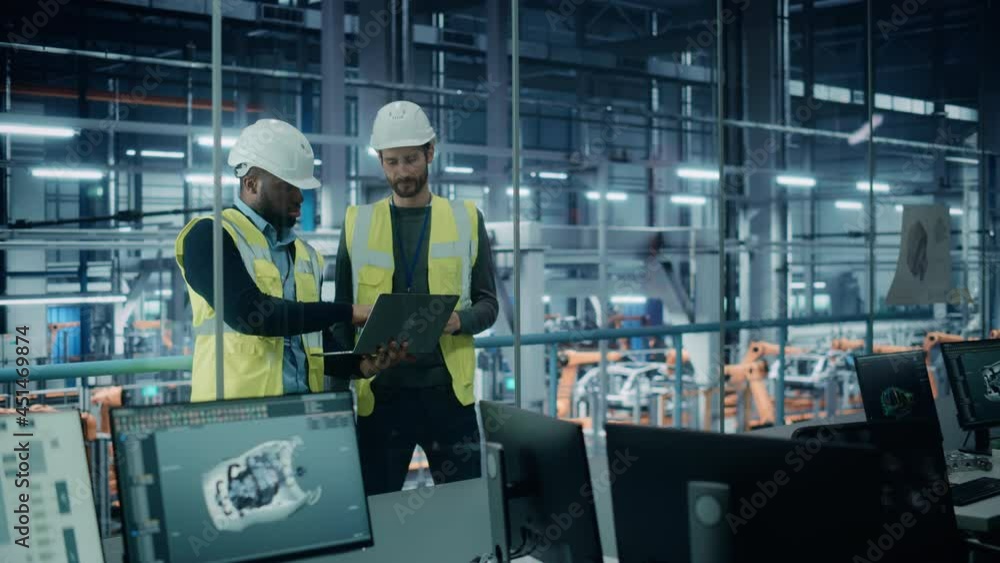 Car Factory: Project Manager and Automotive Engineer in Hard Hat, Talking, Using Laptop. Monitoring, Control, Equipment Production. Automated Robot Arm Assembly Line Manufacturing Electric Vehicles Car Factory: Project Manager and Automotive Engineer in Hard Hat, Talking, Using Laptop. Monitoring, Control, Equipment Production. Automated Robot Arm Assembly Line Manufacturing Electric Vehicles