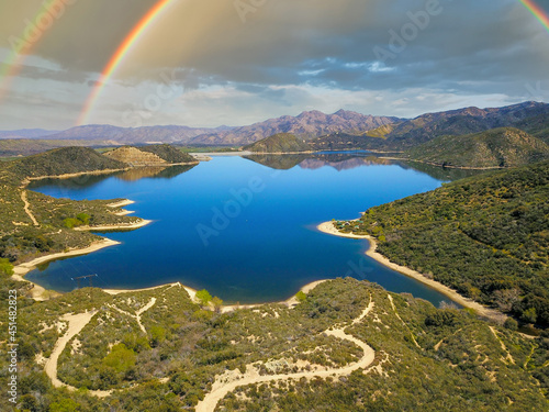 a majestic aerial panoramic shot of the vast blue still lake water with breathtaking mountain ranges reflecting off the lake with a rainbow at Silverwood Lake in Hesperia California USA photo