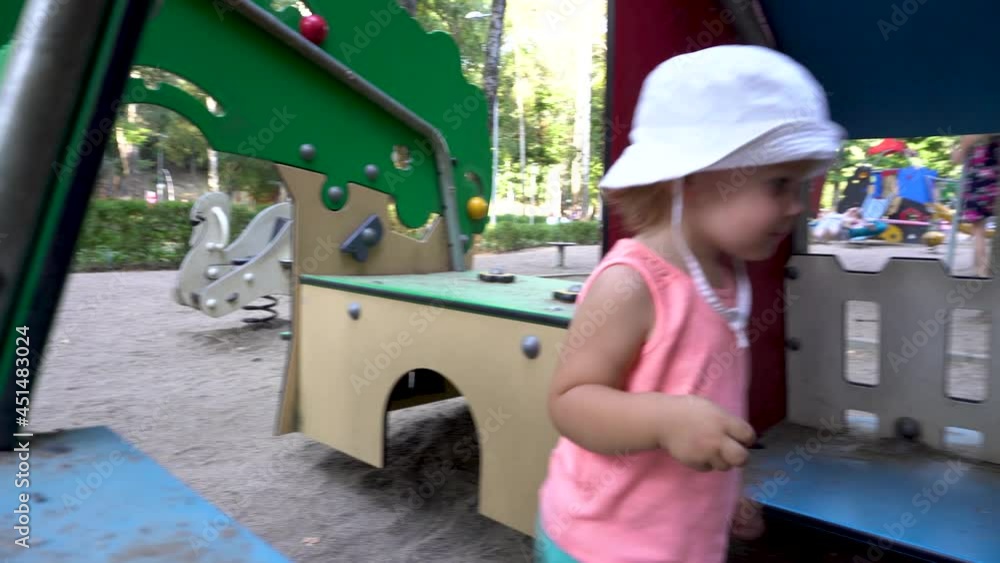 Little girl plays in the playground. On the head is a white panama. Pink T-shirt. Kindergarten. City Park. Summer day. Little girl plays in the playground. On the head is a white panama. Pink T-shirt. Kindergarten. City Park. Summer day.