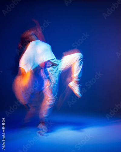 Dancing girl in white sportswear in neon studio light. Female dancer show expressive hip hop dance. Long exposure