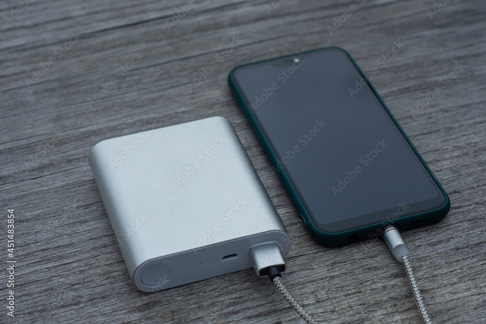 Power Bank charges a smartphone on a wooden bench in the park. Power Bank charges a smartphone on a wooden bench in the park.