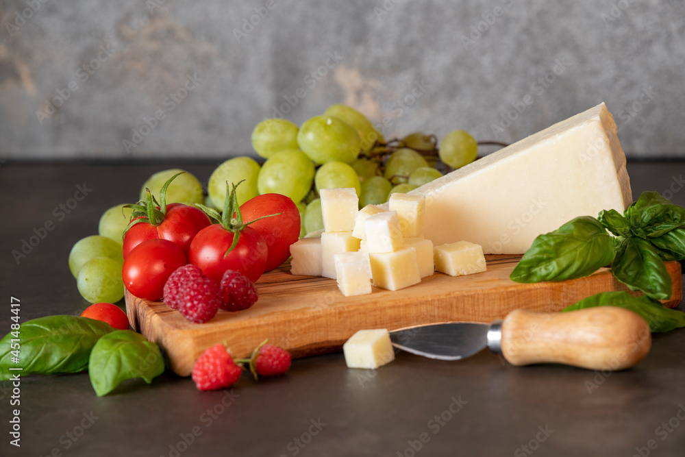 tomatoes, cheese, basil, raspberries and grapes on an olive board on a dark background tomatoes, cheese, basil, raspberries and grapes on an olive board on a dark background