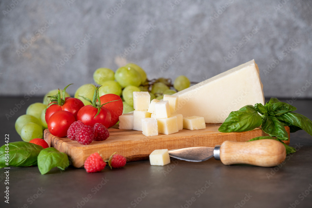 tomatoes, cheese, basil, raspberries and grapes on an olive board on a dark background tomatoes, cheese, basil, raspberries and grapes on an olive board on a dark background